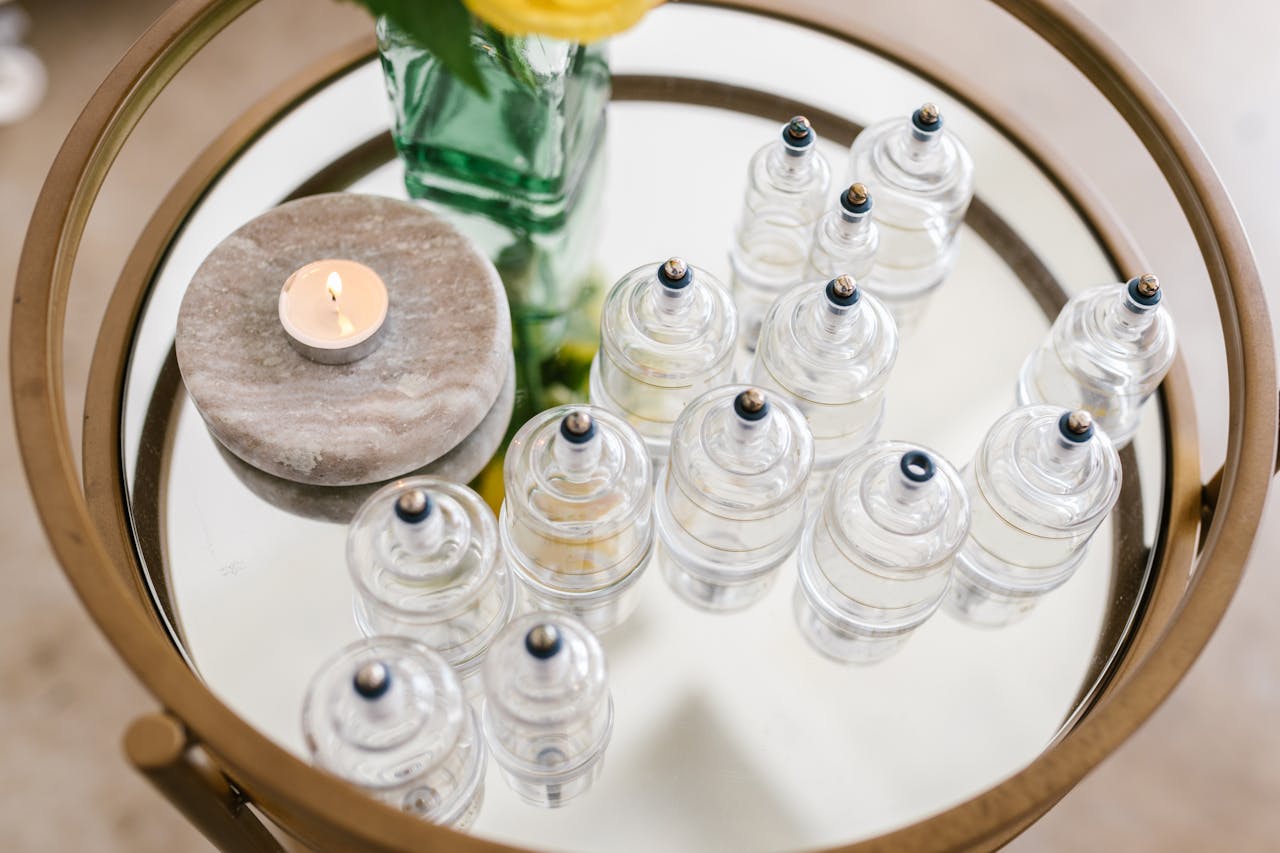 A stylish arrangement of glass cupping jars on a mirrored table with a candle and flowers, ideal for spa settings.